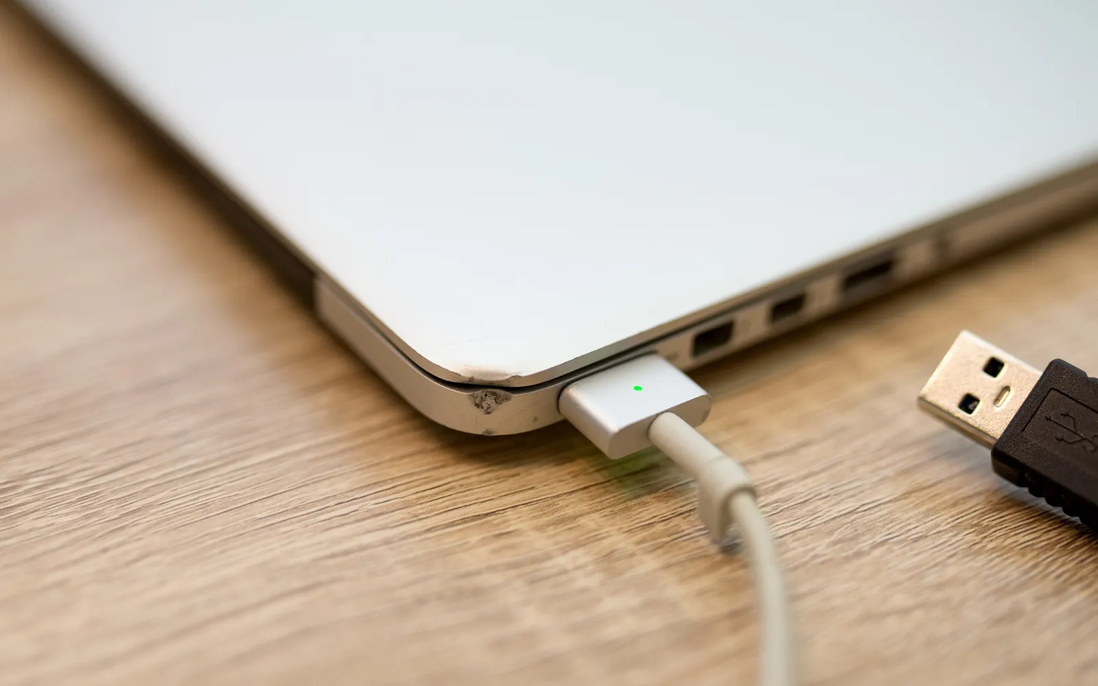 A laptop on a wooden table with a USB cable next to it